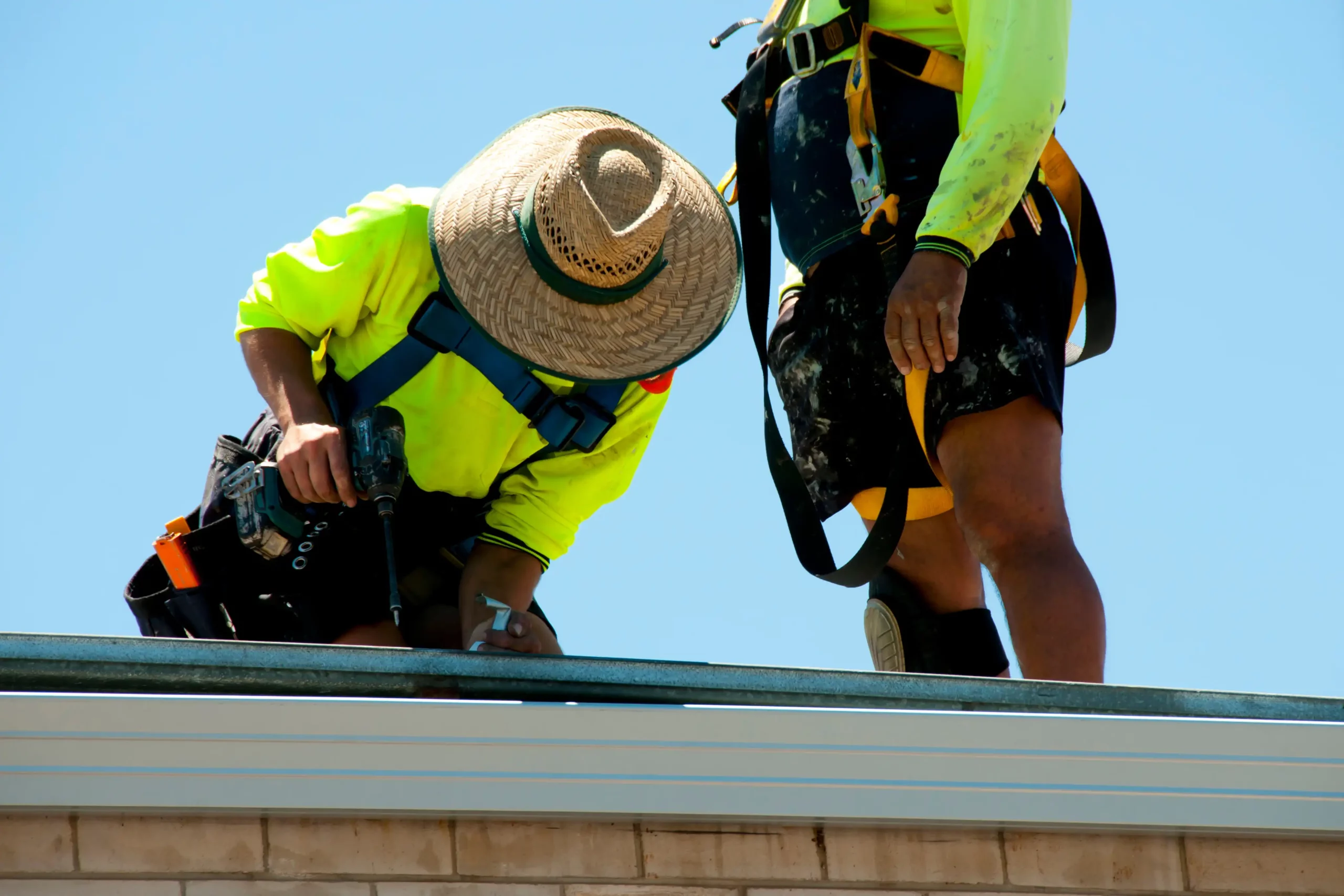 Construction workers wearing high-visibility gear and safety equipment working on roof installation in Australia